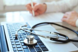 A doctor is writing and a stethoscope on the laptop